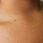 A close up of a neck wearing a yellow gold 14K Gold Asymmetrical Birthstone Necklace - Emerald (May). 