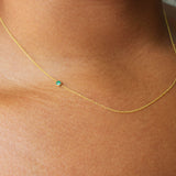 A close up of a neck wearing a yellow gold 14K Gold Asymmetrical Birthstone Necklace - Emerald (May). 