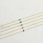 Five yellow gold 14K Gold Asymmetrical Birthstone Necklaces - Tanzanite (December), Turquoise (December), Emerald (May), Citrine (November) and Garnet (January) laid on a white background. 