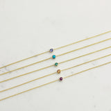 Five yellow gold 14K Gold Asymmetrical Birthstone Necklaces - Tanzanite (December), Turquoise (December), Emerald (May), Citrine (November) and Garnet (January) laid on a white background. 