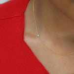 A close-up of a neck wearing a yellow gold 14K Gold Asymmetrical Birthstone Necklace - Opal (October), styled in a red top. 