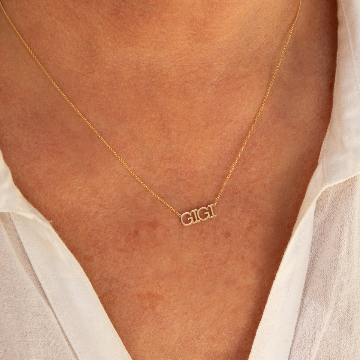 Close-up of a décolletage wearing a GIGI Necklace in yellow gold with a cable chain, with a white shirt. 