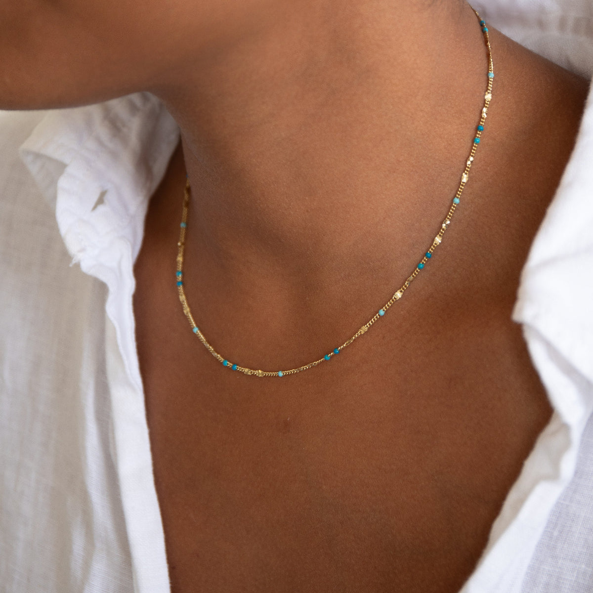 A close-up of a neck wearing a Confetti Necklace - Blue, styled in a white shirt. 