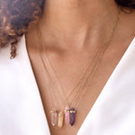 A close-up of a woman's neck wearing Retreat Necklaces (Clarity, Happiness, Healing and Love), with curly brown hair and a white top. 

