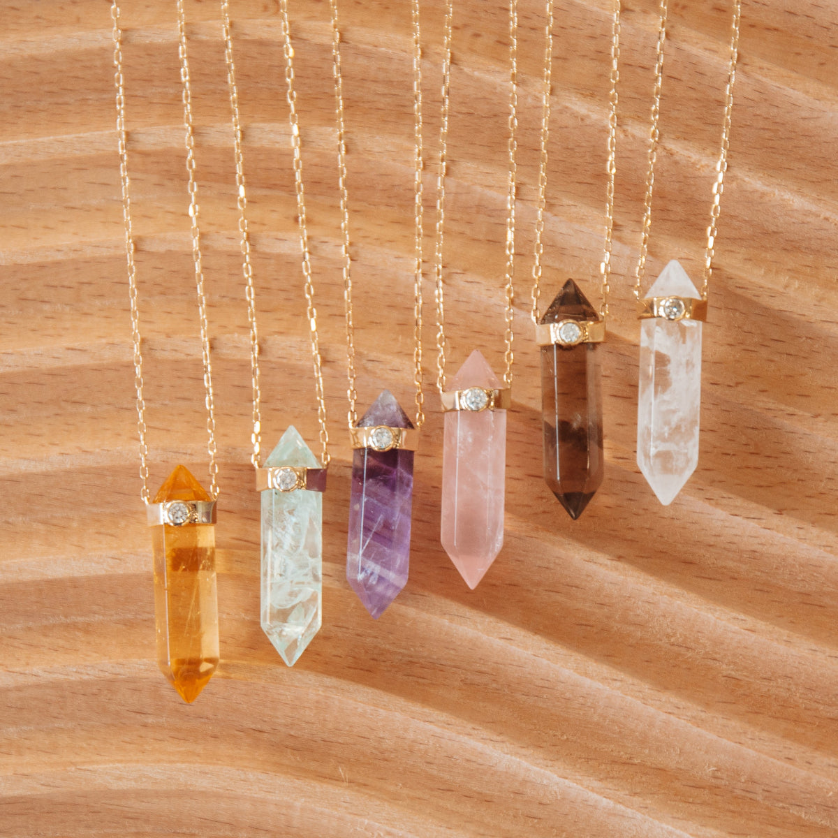 Six Retreat Necklaces (Happiness, In Flow, Healing, Love, Courage and Clarity) on a wooden background. 