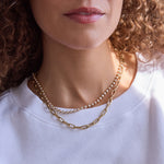 Close-up of a person's neck wearing The Ultimate Diamond Necklace and a Bold Link Chain, with a white t-shirt and brown curly hair. 