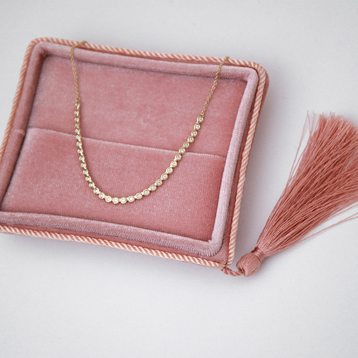 The Everyday Diamond Necklace in a pink holder against a light grey background. 