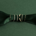Two 4 Diamond Rings, three Pave Diamond Rings and an Open Diamond Ring on a dark green ribbon against a green background. 