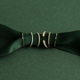 Two 4 Diamond Rings, three Pave Diamond Rings and an Open Diamond Ring on a dark green ribbon against a green background. 