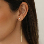 A close-up of a Pearl Drift Threader worn on a woman's ear, with brown hair against a blurred white background.