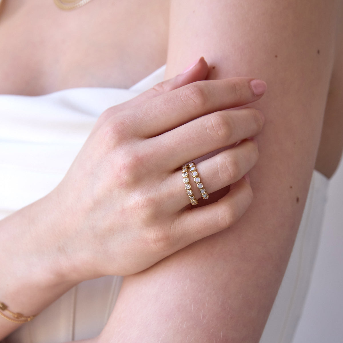 A woman's hand wearing The Magnolia Bouquet Ring and The Evermore Ring, with a white strapless top. 