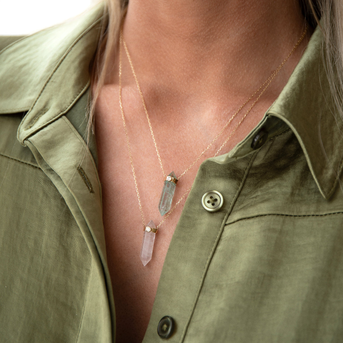 Close-up of a décolletage wearing two The Retreat Necklaces in In Flow and Clarity, styled in a khaki green shirt. 