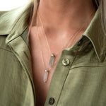 Close-up of a décolletage wearing two The Retreat Necklaces in In Flow and Clarity, styled in a khaki green shirt. 