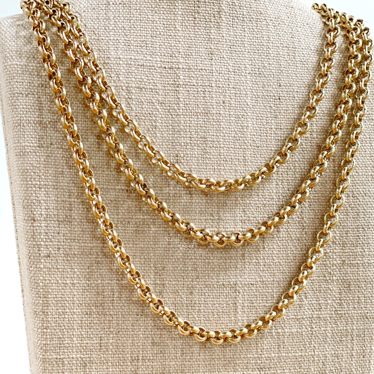 Three yellow gold Rolo Necklaces on a textured beige background.
