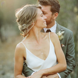 Couple embracing outdoors with the woman wearing a Zodiac Necklace - Libra and a Simple Bangle with a blurred natural background. 