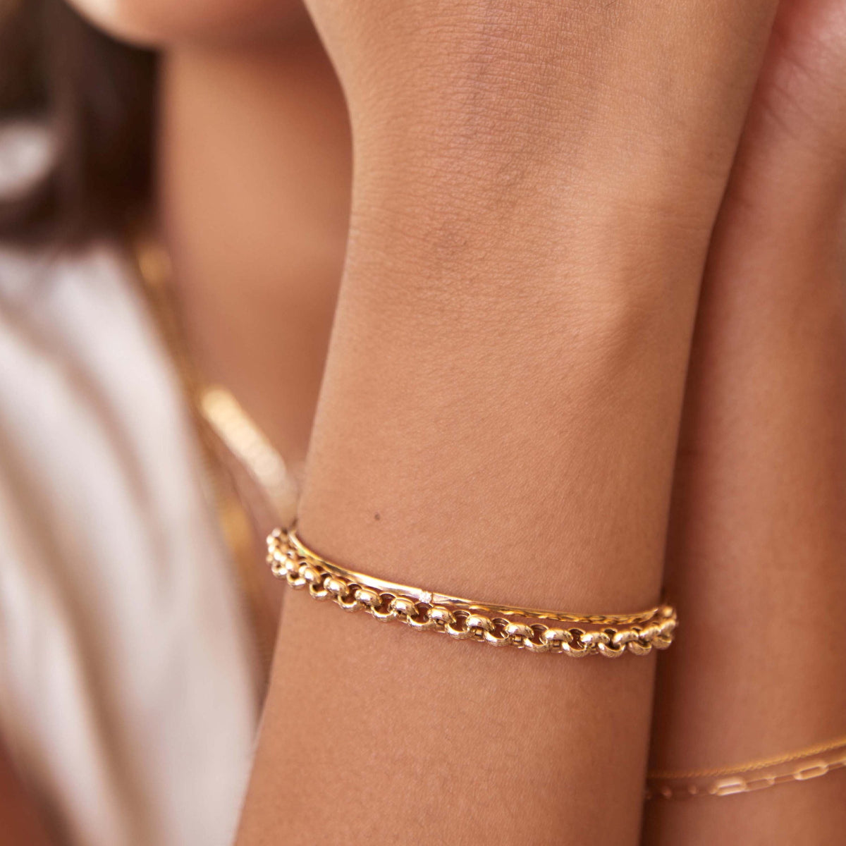 A close-up of a woman’s arms wearing several yellow gold bracelets, including a Rolo Bracelet, an Off the Cuff Bracelet and an Element Short Link Bracelet.