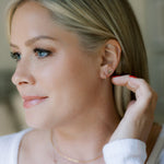 A blonde woman wearing a Lip Stud and a 
Thin Gold Hoop with a white top and blurred background. 