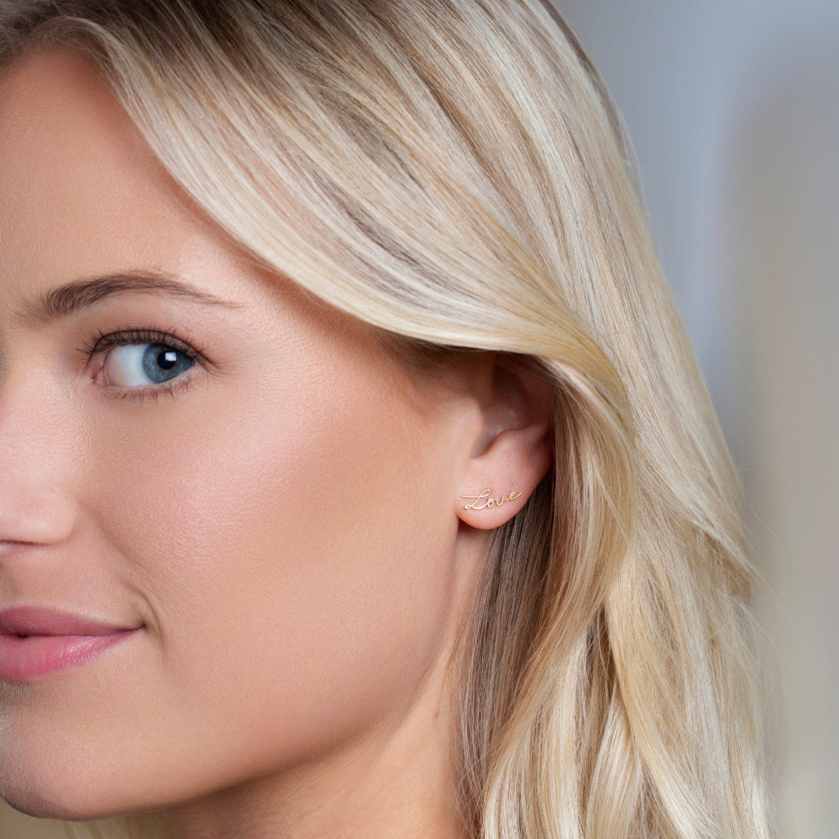 Close-up of a More Love Stud being worn by a blonde woman against a light blurred background. 