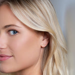 Close-up of a More Love Stud being worn by a blonde woman against a light blurred background. 