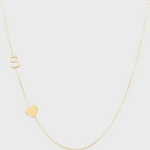 A Monogram Necklace with Heart Yellow Gold and a letter S charm on a light grey background. 