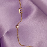 A Monogram Necklace with Diamond and the letter E in yellow gold, against light purple silk fabric as the background.