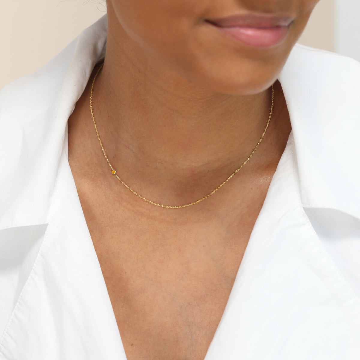 A close-up of a woman’s neck wearing a yellow gold 14K Gold Asymmetrical Birthstone Necklace - Citrine (November), styled in a white shirt. 