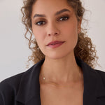 A woman wearing a yellow gold 14k Gold Asymmetrical Charm Necklace - Pavé Hamsa with a cable chain styled  which a black blazer against a white background. 