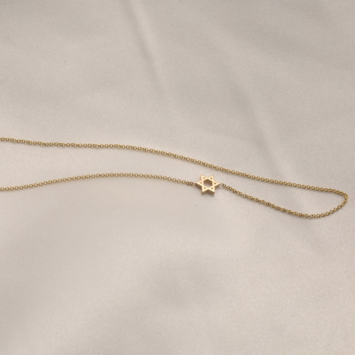 A yellow gold cable chain 14k Gold Asymmetrical Charm Necklace - Star of David against a light grey fabric background.