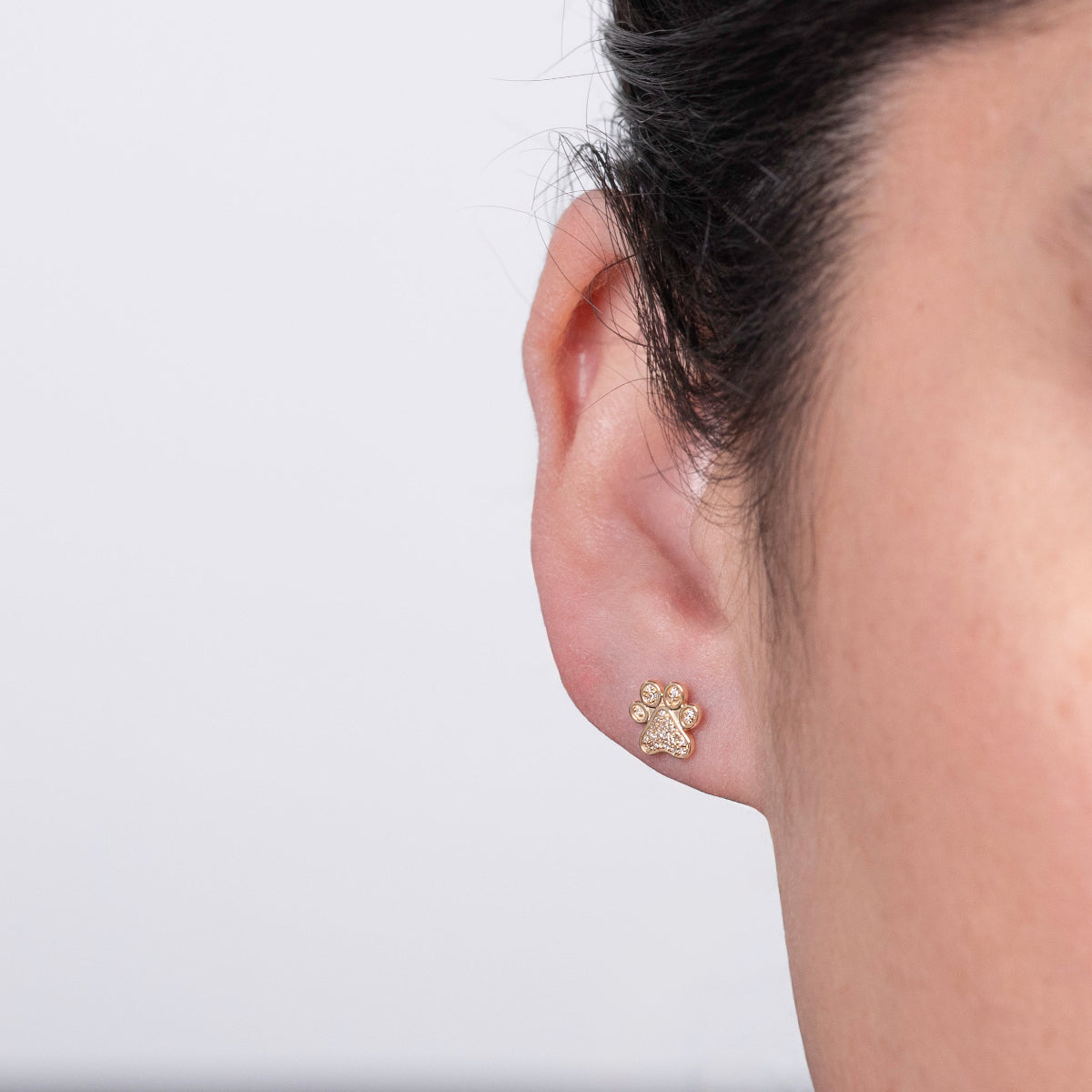 Close-up of a Pavé Charm Stud - Paw in a woman's ear against a light grey background. 