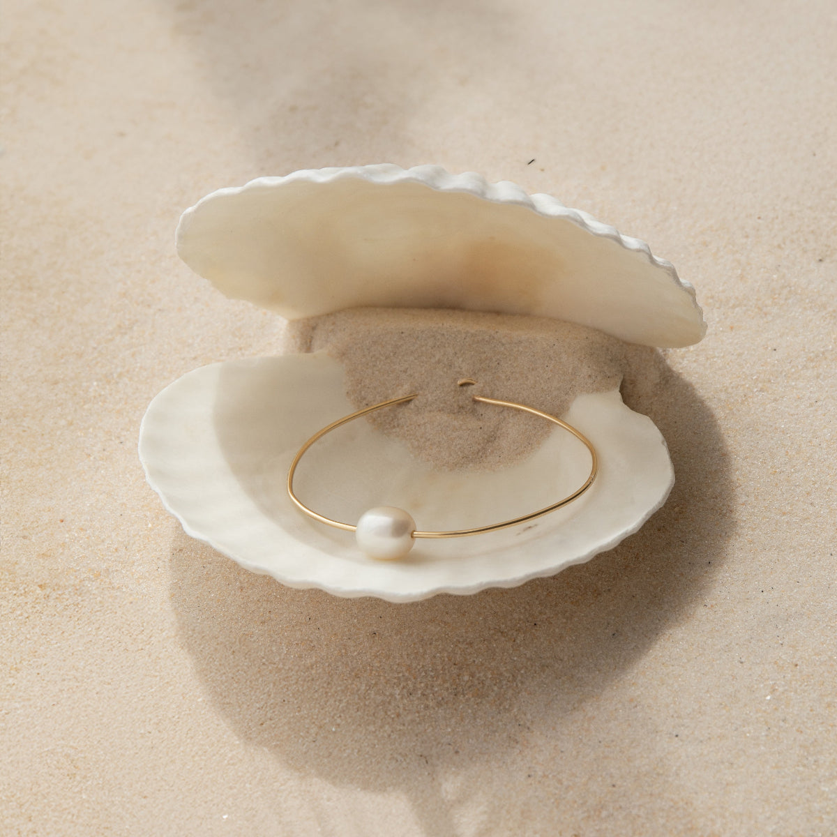A Baroque White Pearl Bangle in a white shell on a beige background. 