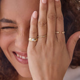 Close-up of a woman with her hand wearing a Perla Pinky Ring, Delicate Band, Pave Diamond Ring and Open Diamond Ring in front of her face. 
