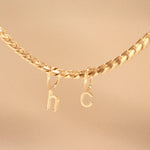A yellow gold necklace with Petite Letter Charms in h and c on against a beige background.