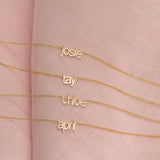 Four Petite Nameplate Necklaces in yellow gold, in the names Josie, Tay, Chloe and April (all in lowercase) on a pink fabric background. 