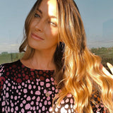 Fran Newman Young wearing a Pisces zodiac necklace, paired with a black top featuring pink and dark red spots, set against an outdoor background.