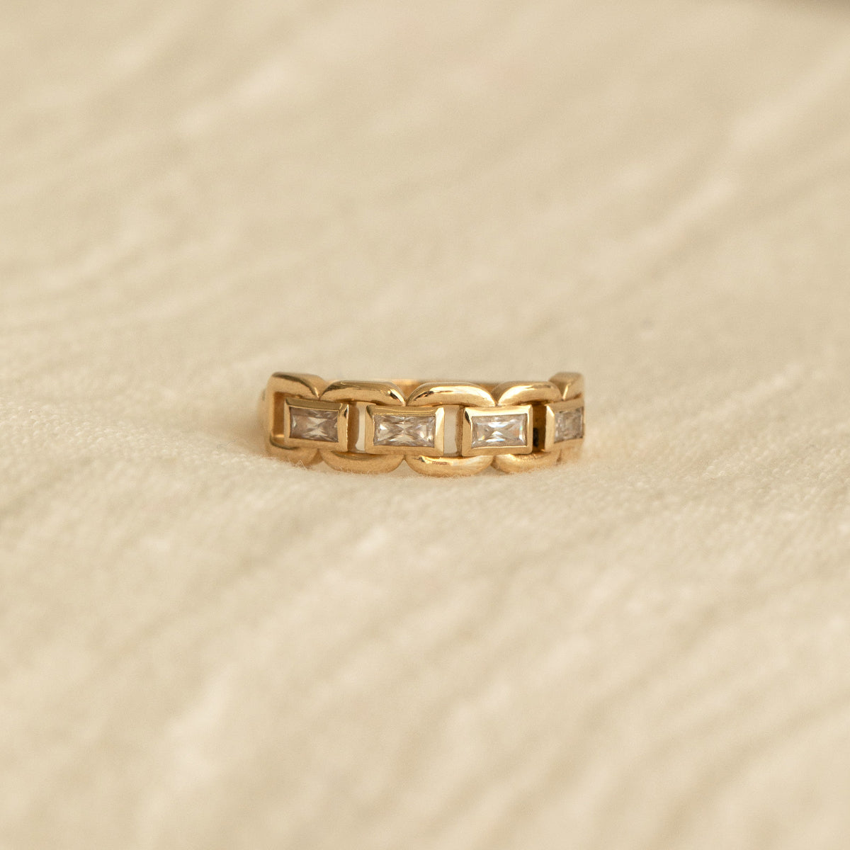 A yellow gold C'est Moi Link Ring on a beige fabric background. 