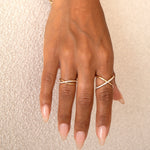 A hand wearing a yellow gold Criss-Cross Diamond Duo Ring and Criss-Cross Diamond Daze Ring against a cream background. 
