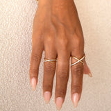 A hand wearing a yellow gold Criss-Cross Diamond Duo Ring and Criss-Cross Diamond Daze Ring against a cream background. 