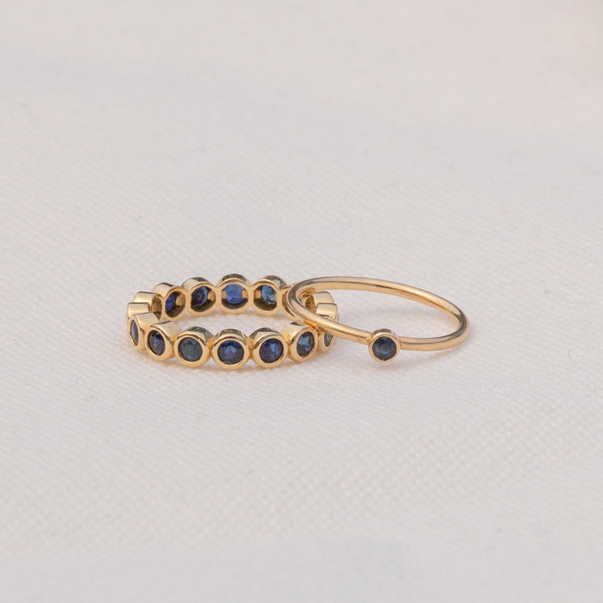 A Birthstone Ring in Sapphire - September and The Iris Bouquet Ring in yellow gold against a light grey background. 