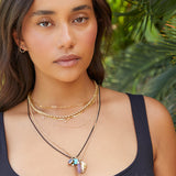 A woman wearing multiple necklaces, including a Custom Gold Necklace with four letters, an Element Short Link Chain, a Rolo Necklace, a Black Rhodium Antique Beach Chain and a Round Curb Chain with a Diamond Heart Locket, an Etched Turquoise Heart Charm and a Balance Crystal Charm, along with Open Eclipse Earrings and a black top.