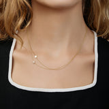 A close-up of a woman's neck wearing two yellow gold 14k Gold Asymmetrical Charm Necklaces (one star and one pavé star), styled with a black and white top. 