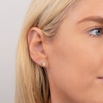 Close-up of a yellow gold Charm Stud - Paw in a blonde woman's ear with a light grey background. 