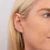 Close-up of a yellow gold Charm Stud - Paw in a blonde woman's ear with a light grey background. 