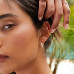 Close-up of a woman wearing a Tres Pearl Earring with blurred palm trees in the background.