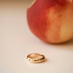 A yellow gold Tube Ring with a peach in the background. 