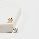 Two Charm Studs - Paw, one in yellow gold and one in white gold, against a white background. 