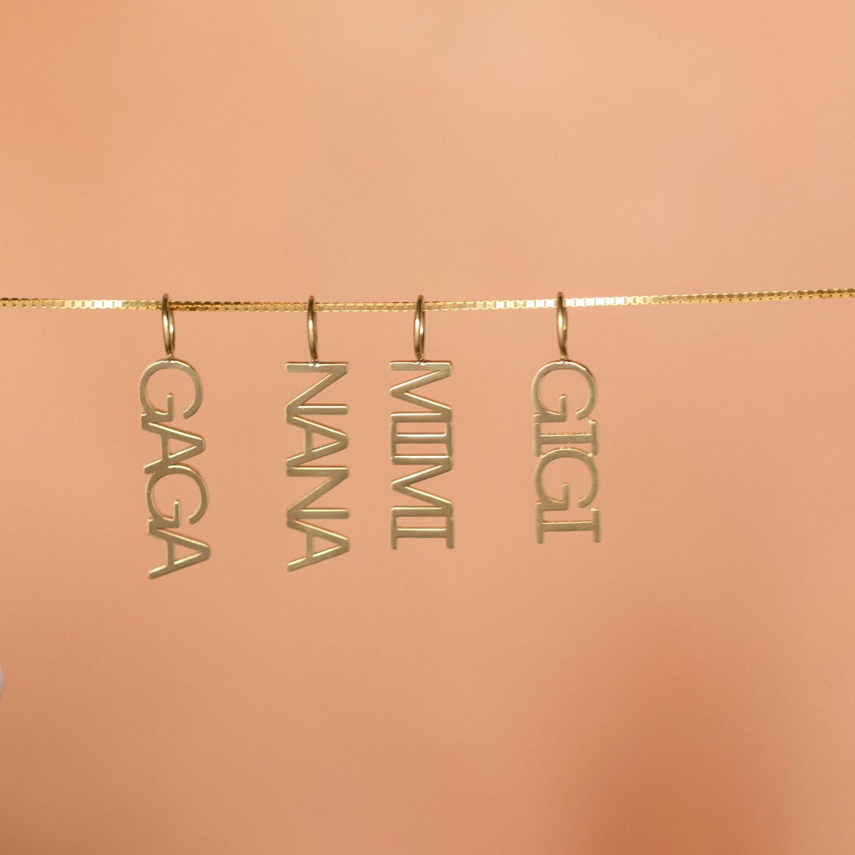 Gold name charms hanging from a string against a peach background