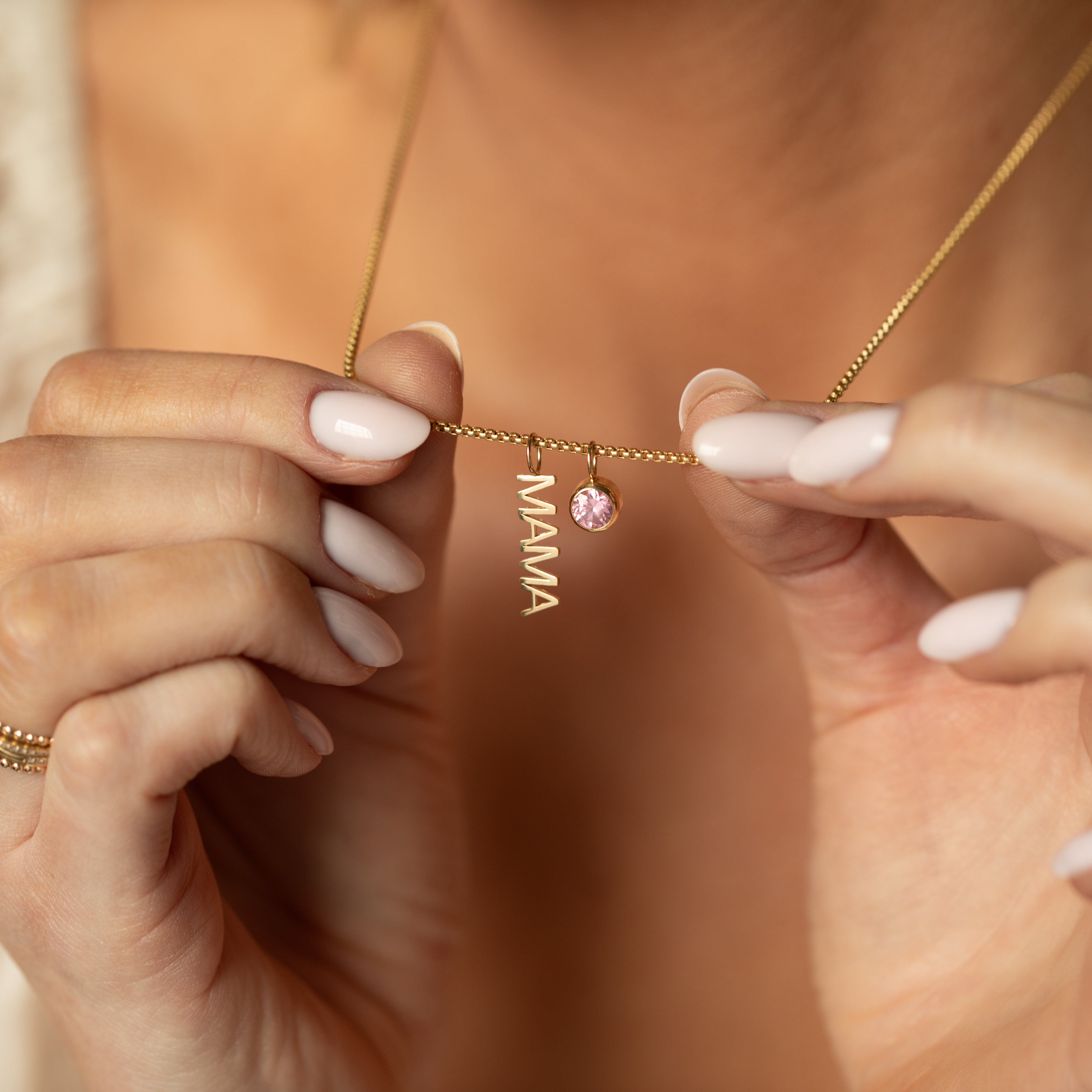 Gold necklace with 'MAMA' pendant held by a person