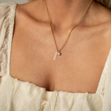 Gold necklace with a 14k gold 'mama' pendant styled with a light pink gemstone pendant on a person wearing a light-colored top.