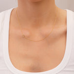 Gold necklace with a small horseshoe charm on a person wearing a white top against a neutral background