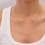 Gold necklace with a small pavé diamond horseshoe charm  on a person wearing a white top against a neutral background